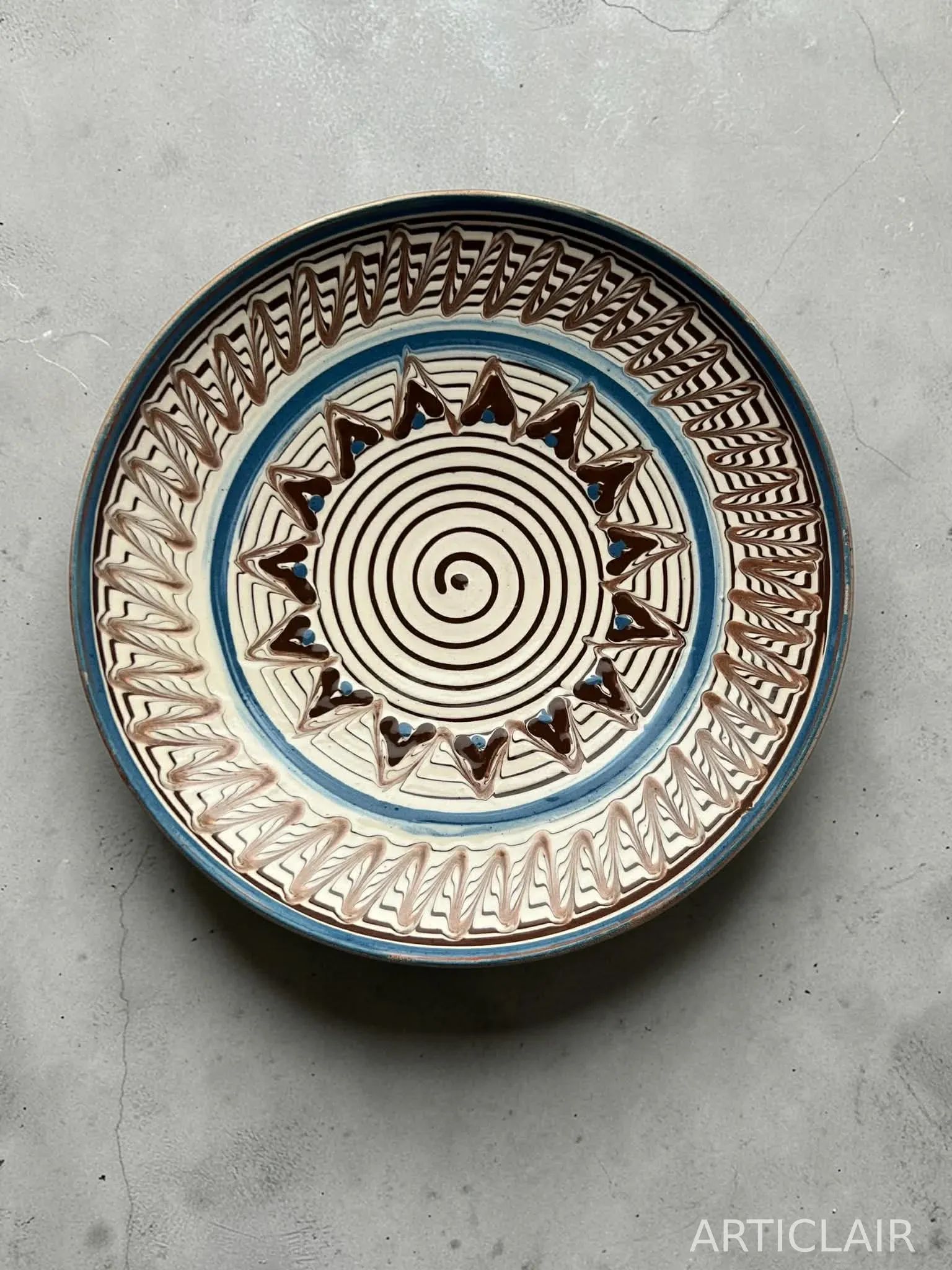 A ceramic plate with a spiral center, blue rim, and zigzag border