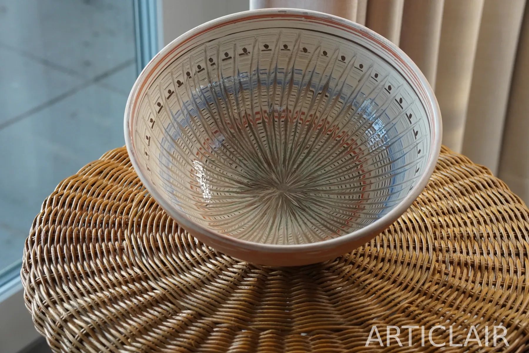A wide Horezu bowl with soft green and red rings on a woven surface
