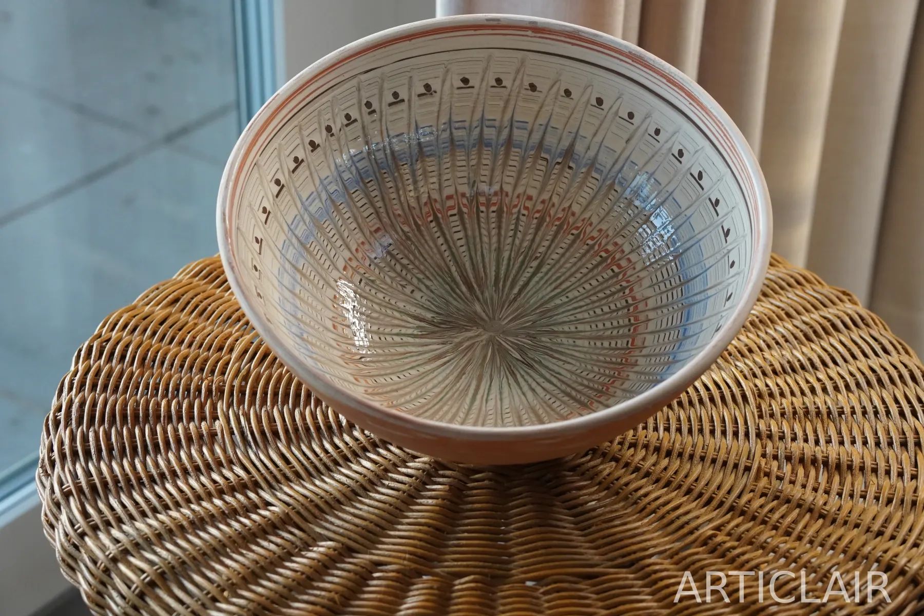 A wide Horezu bowl with soft green and red rings on a woven surface