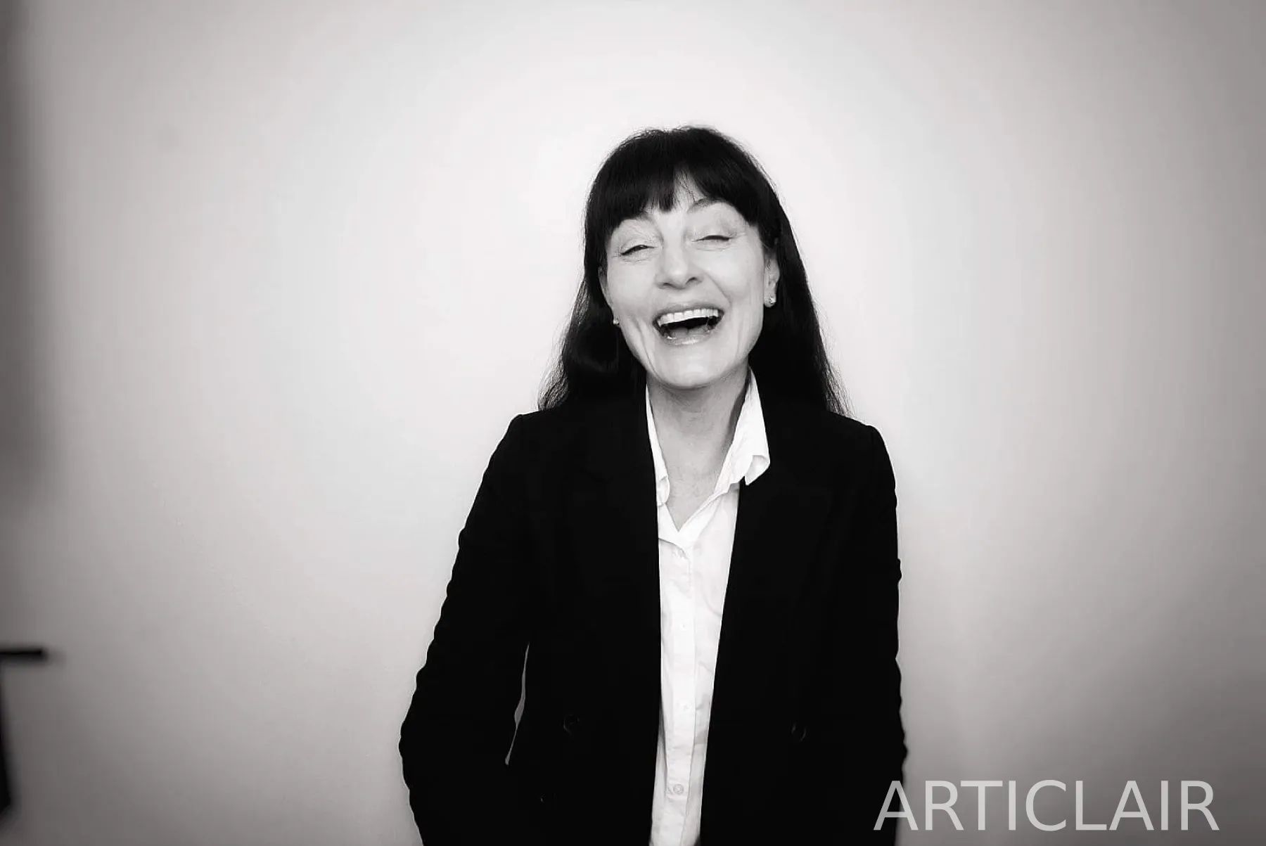 A black-and-white portrait caught mid-laughter against a plain wall